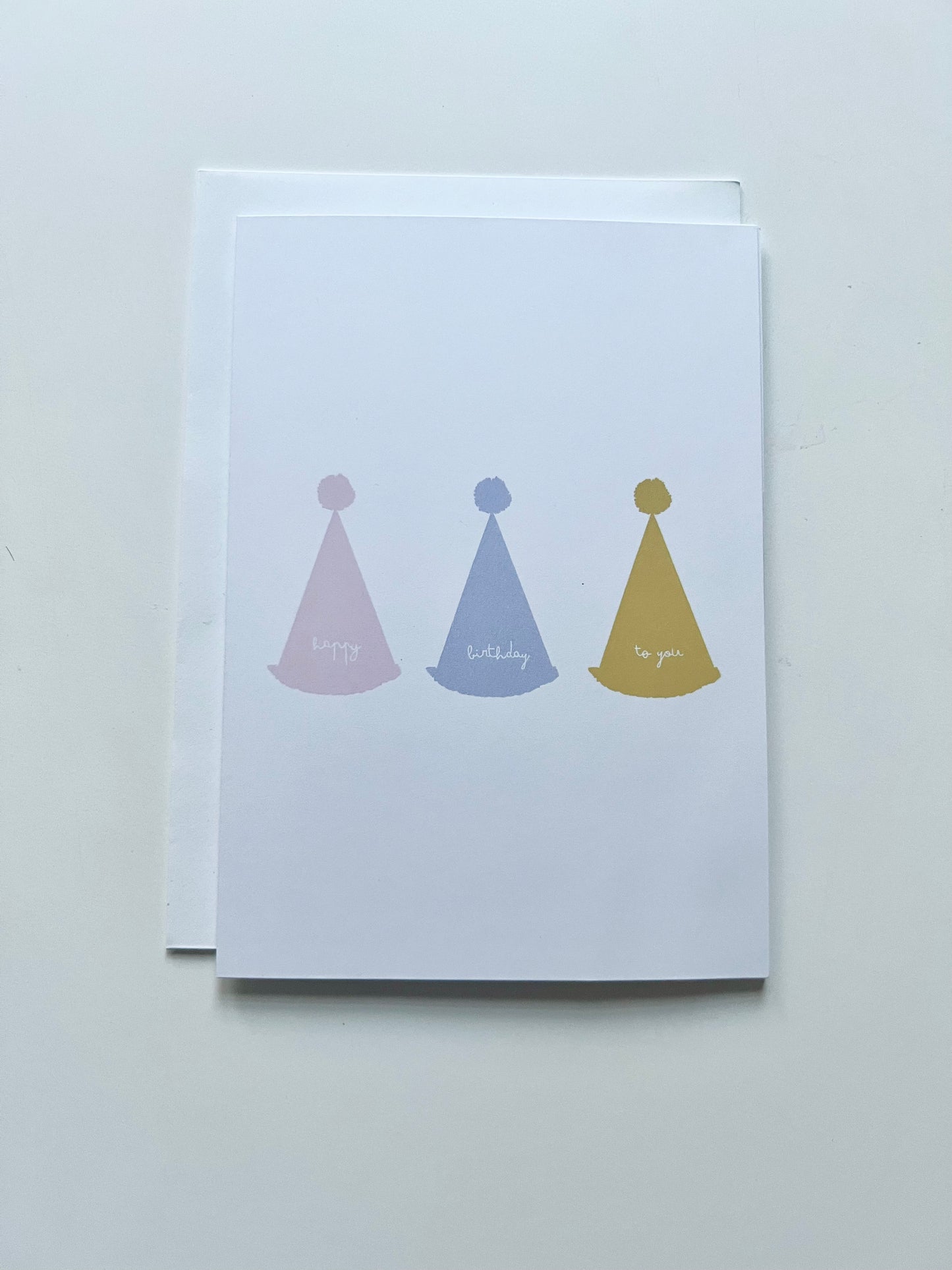 hand drawn greeting card with white background and pink blue and yellow party hats that say happy birthday to you.