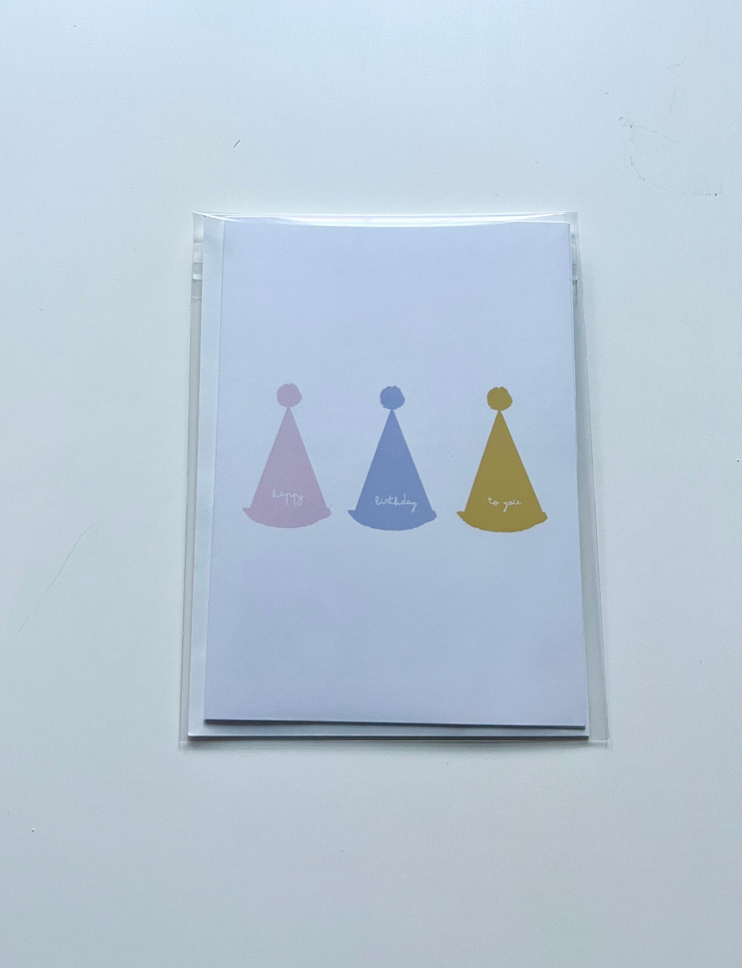 hand drawn greeting card with white background and pink blue and yellow party hats that say happy birthday to you.