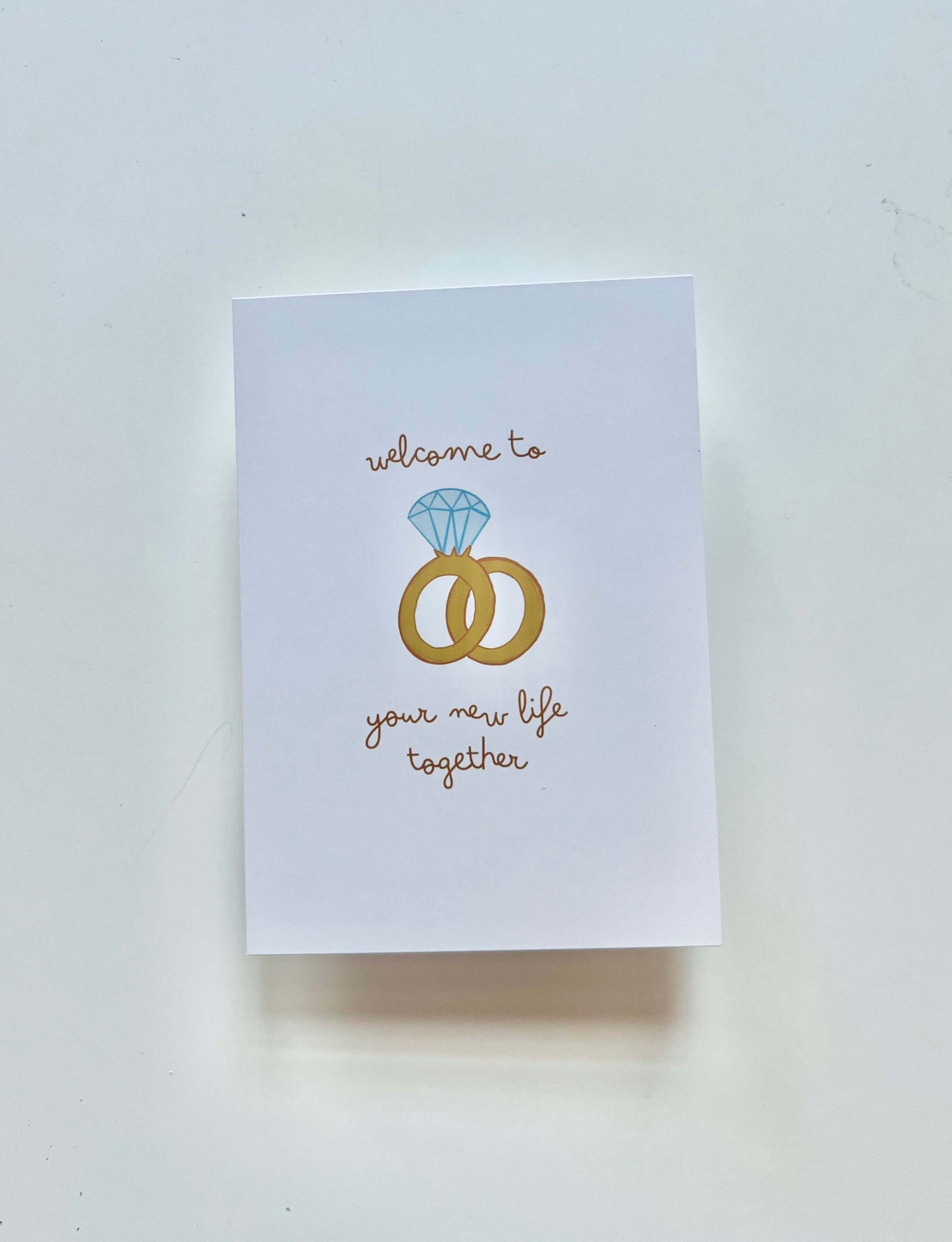 hand drawn greeting card with a diamond ring and wedding band that says welcome to your new life together.