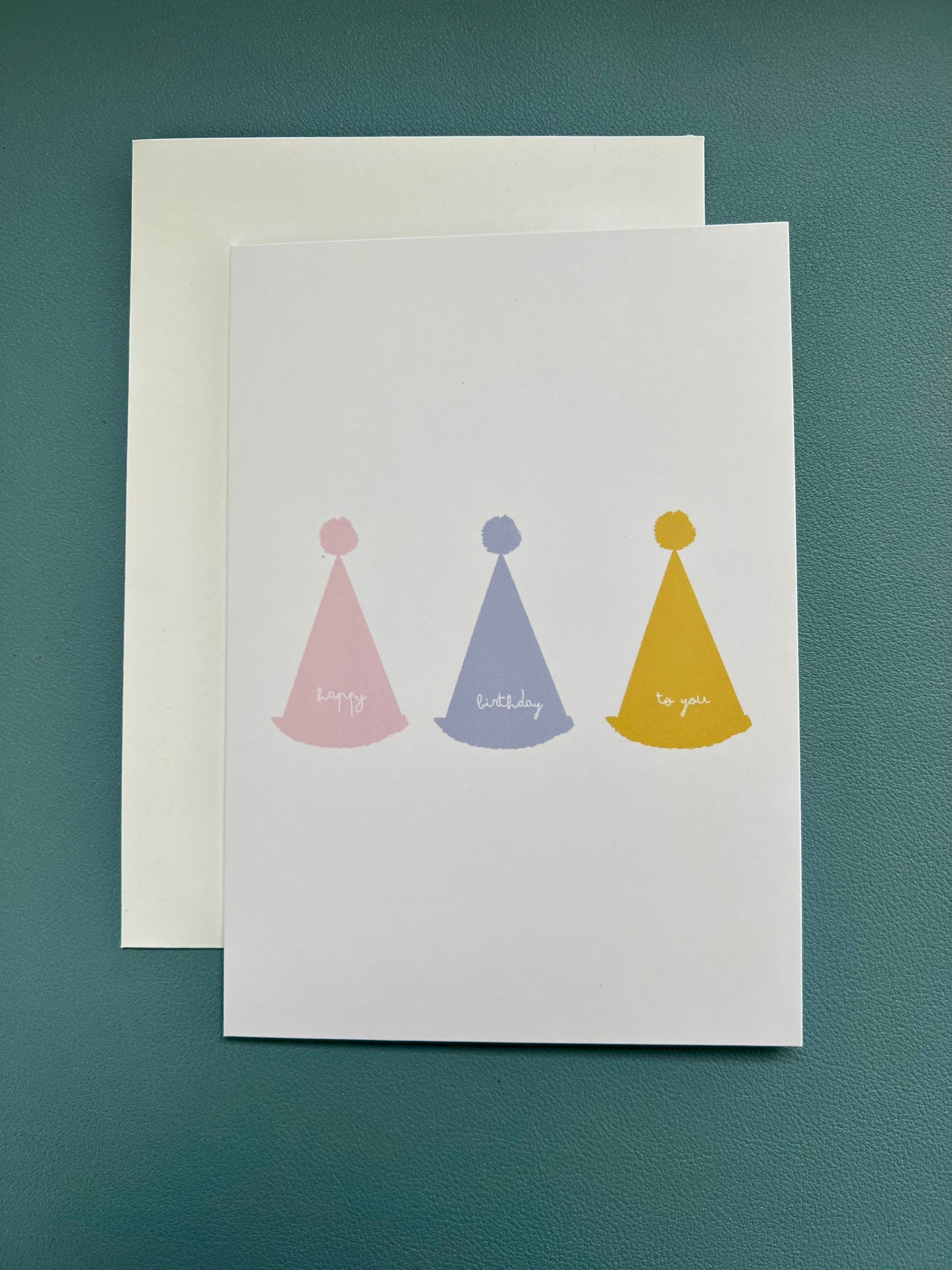 hand drawn greeting card with white background and pink blue and yellow party hats that say happy birthday to you.