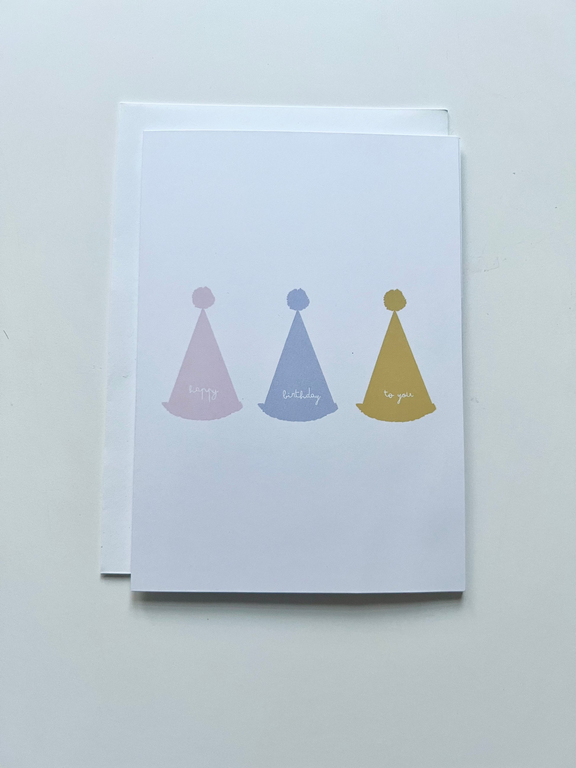 hand drawn greeting card with white background and pink blue and yellow party hats that say happy birthday to you.