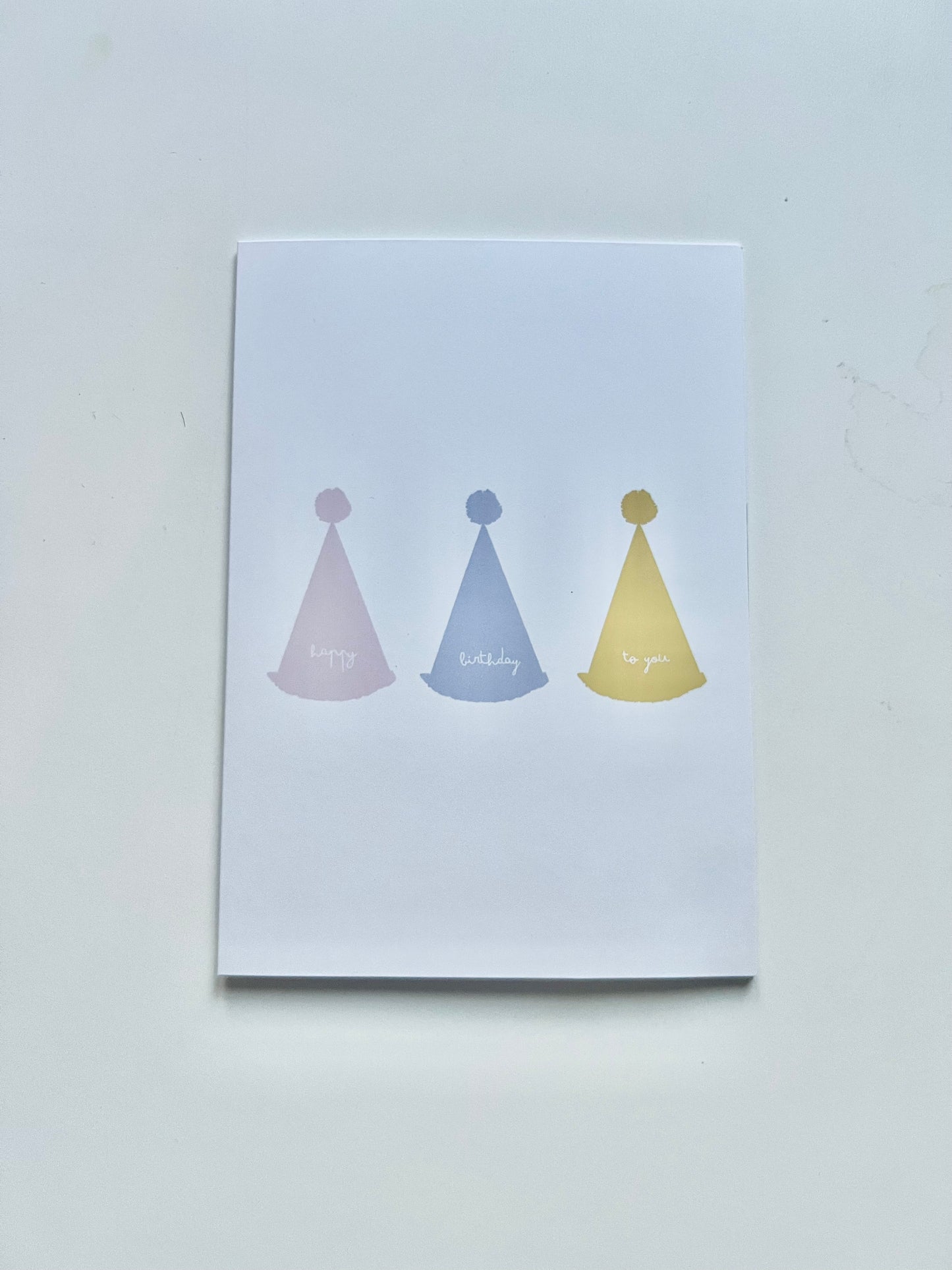 hand drawn greeting card with white background and pink blue and yellow party hats that say happy birthday to you.