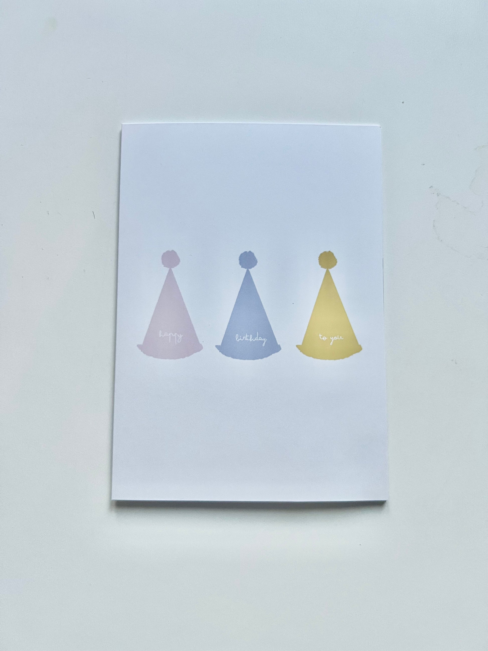 hand drawn greeting card with white background and pink blue and yellow party hats that say happy birthday to you.