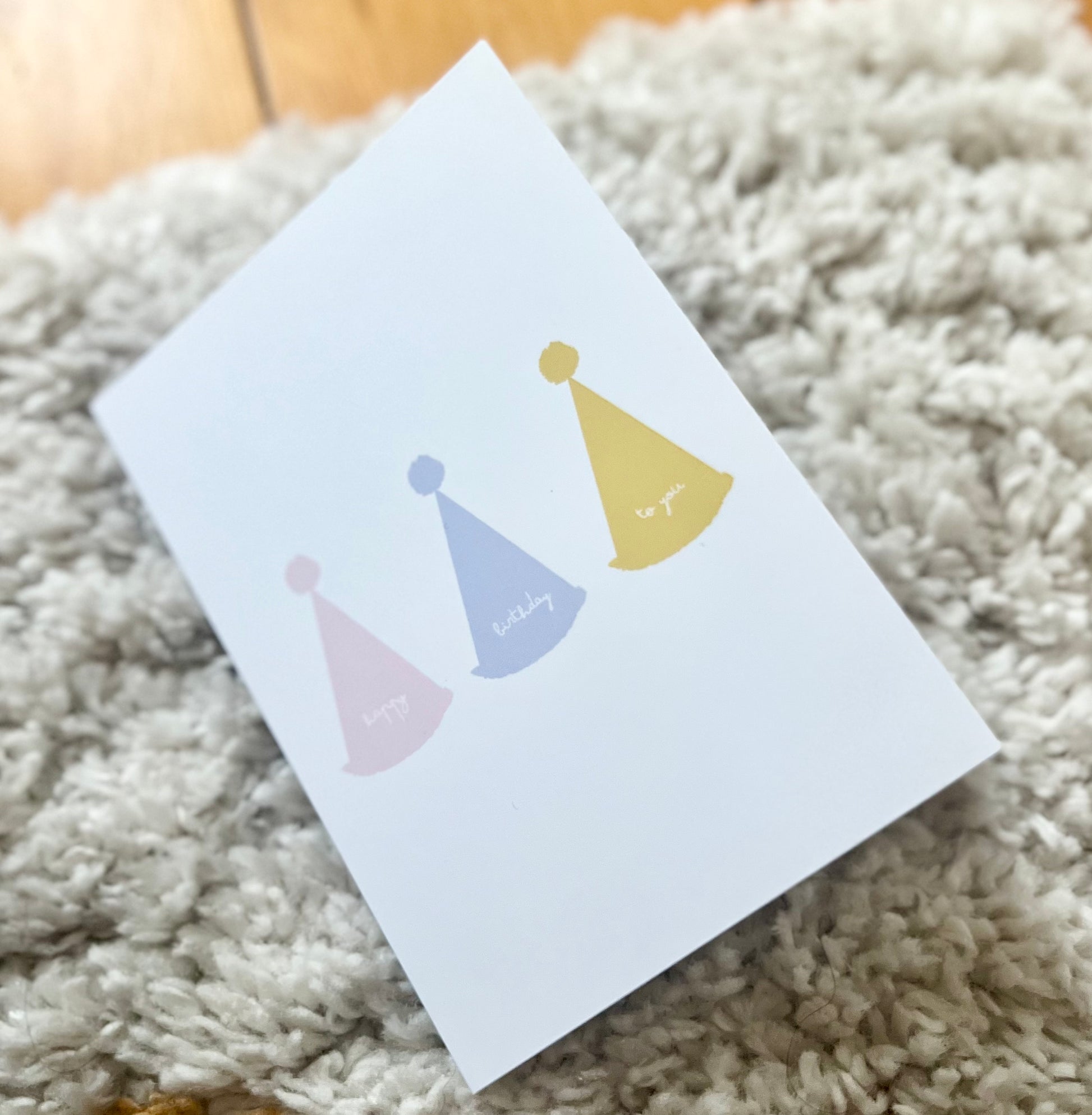 hand drawn greeting card with white background and pink blue and yellow party hats that say happy birthday to you.