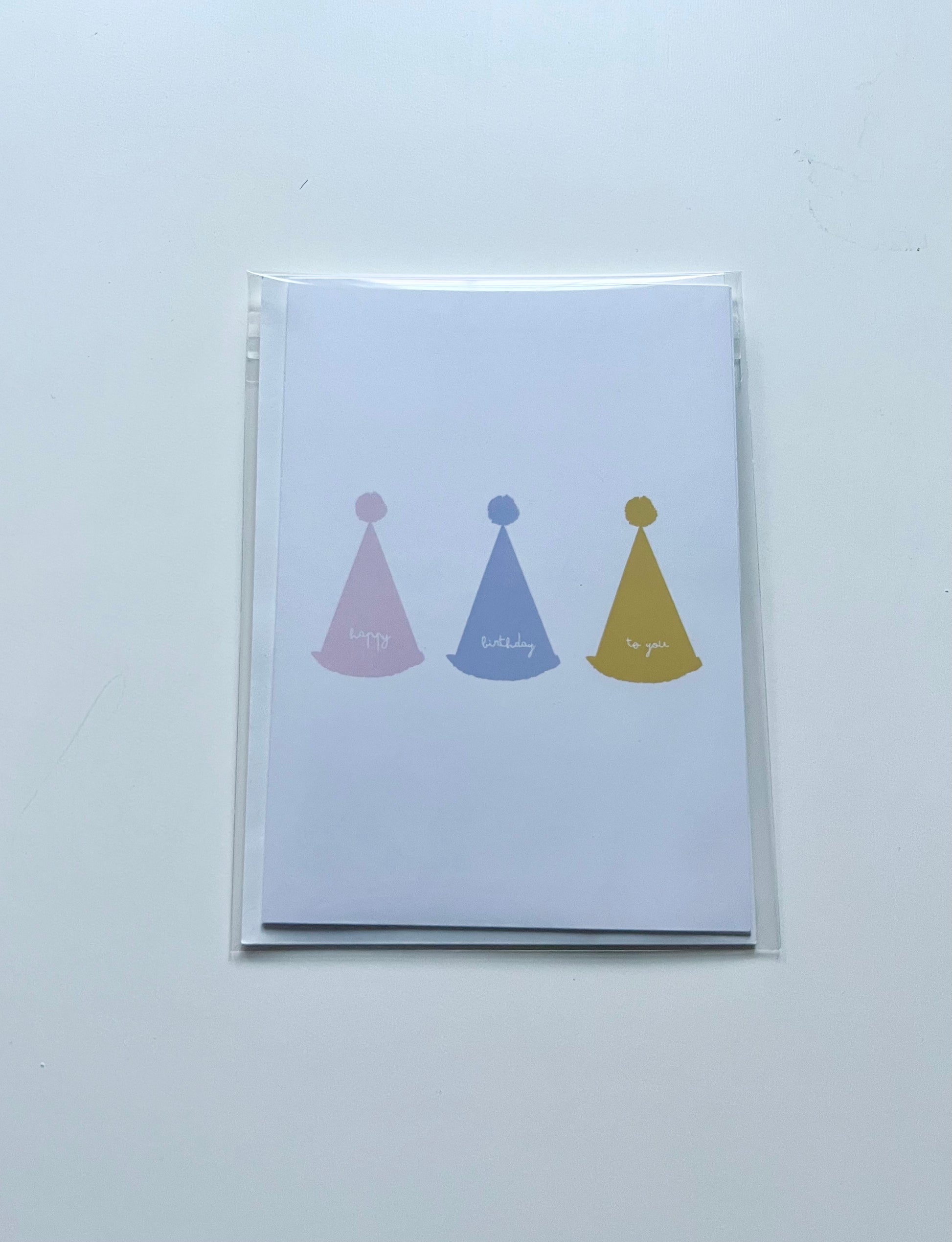 hand drawn greeting card with white background and pink blue and yellow party hats that say happy birthday to you.