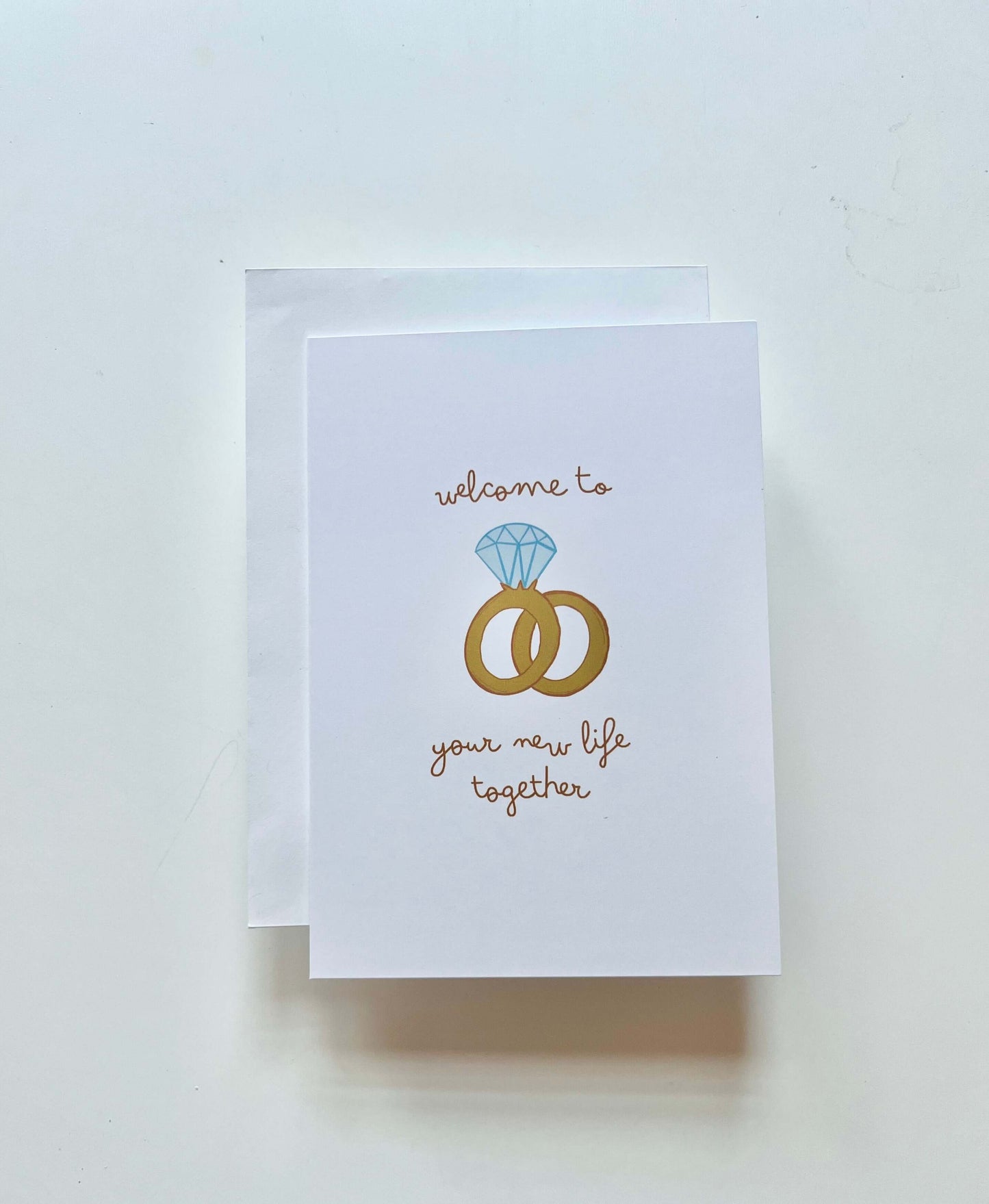 hand drawn greeting card with a diamond ring and wedding band that says welcome to your new life together.