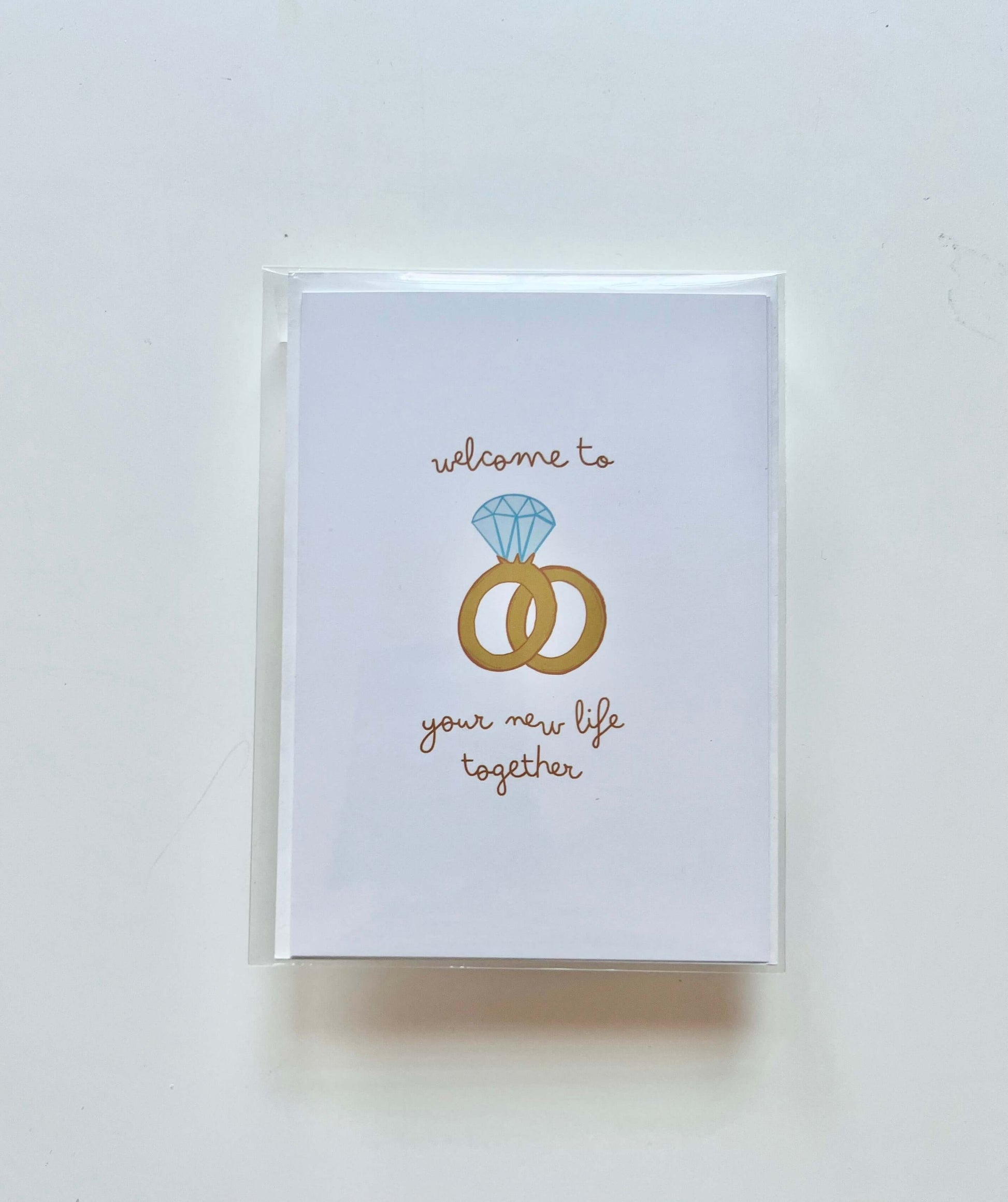 hand drawn greeting card with a diamond ring and wedding band that says welcome to your new life together.