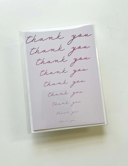 Hand drawn thank you card featuring repeated cursive "thank you" on a pink background, wrapped in clear plastic sleeve.