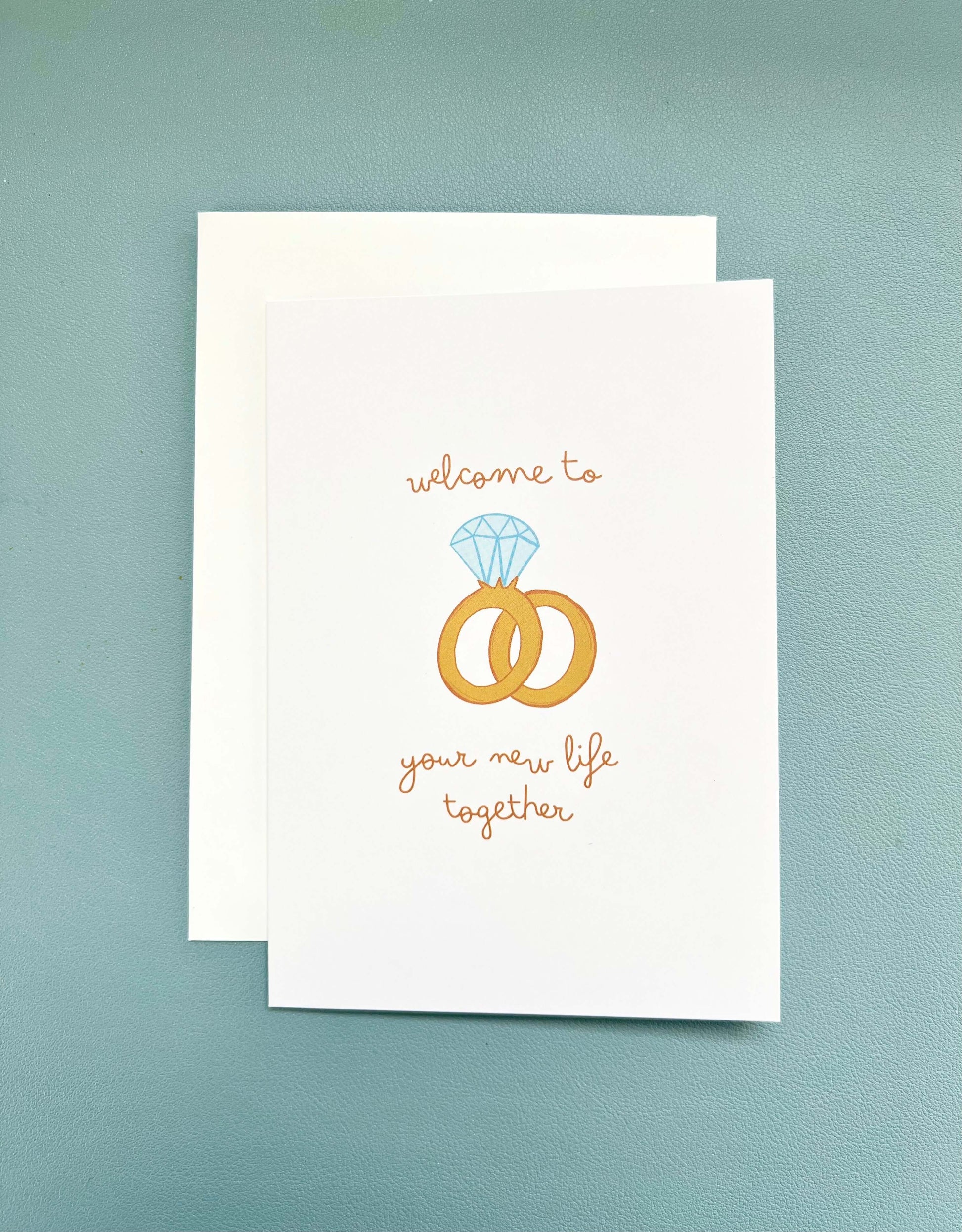 hand drawn greeting card with a diamond ring and wedding band that says welcome to your new life together.