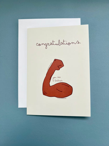 hand drawn yellow encouraging greeting card with a flexed arm that says congratulations you are a badass.